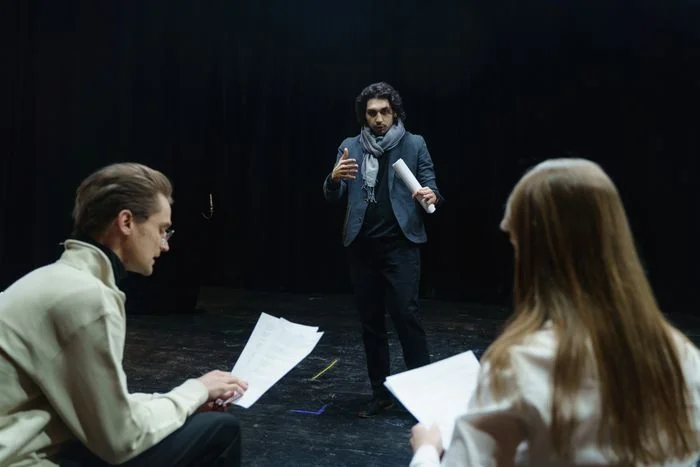 Näyttelijät ja ohjaaja tutkimassa teatterikäsikirjoitusta harjoitussalissa